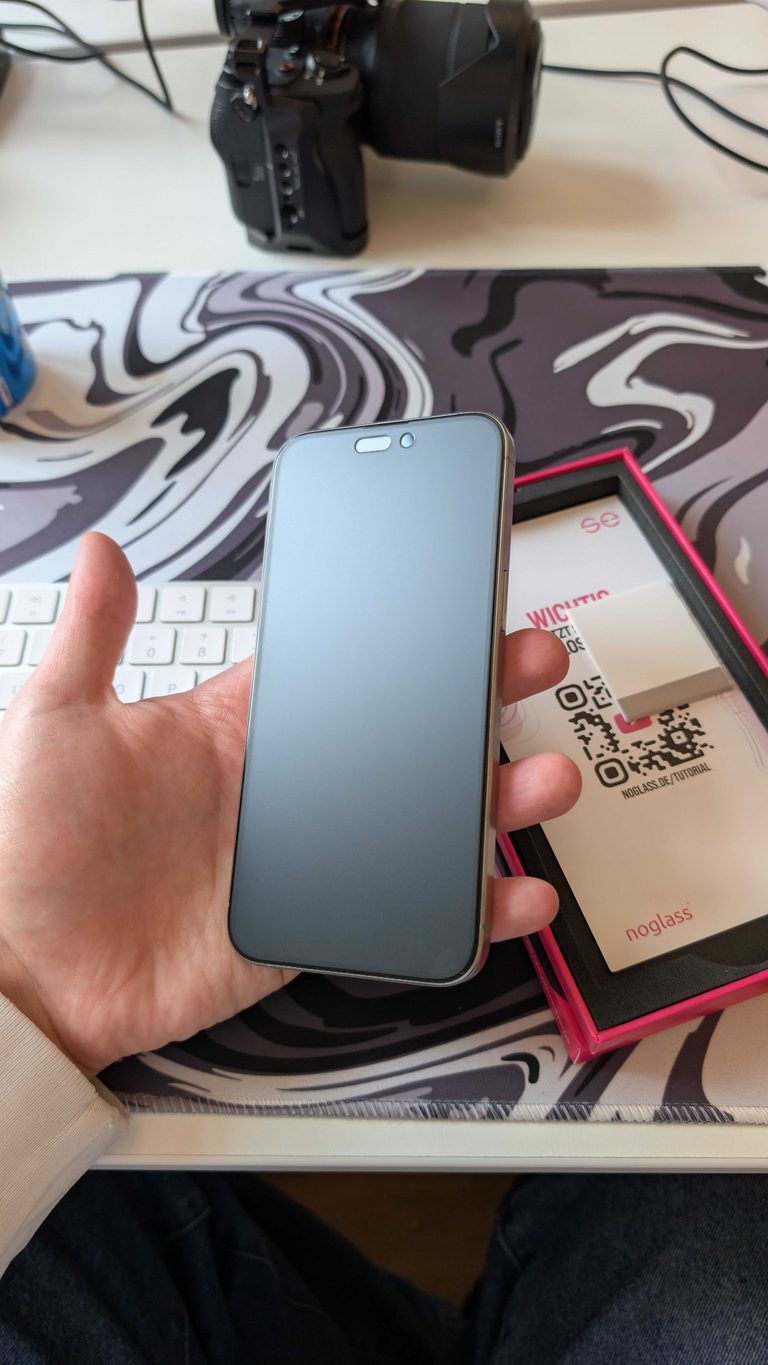 iPhone mit frisch montierter se® noglass Folie in der Hand
